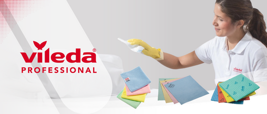 Eine Vileda Professional Anzeige zeigt eine Frau in einem weißen Polo-Shirt und gelben Handschuhen, die ein weißes Reinigungstuch hält. Links daneben ist das Vileda Professional Logo zu sehen. Im Vordergrund befinden sich mehrere bunte Reinigungstücher.