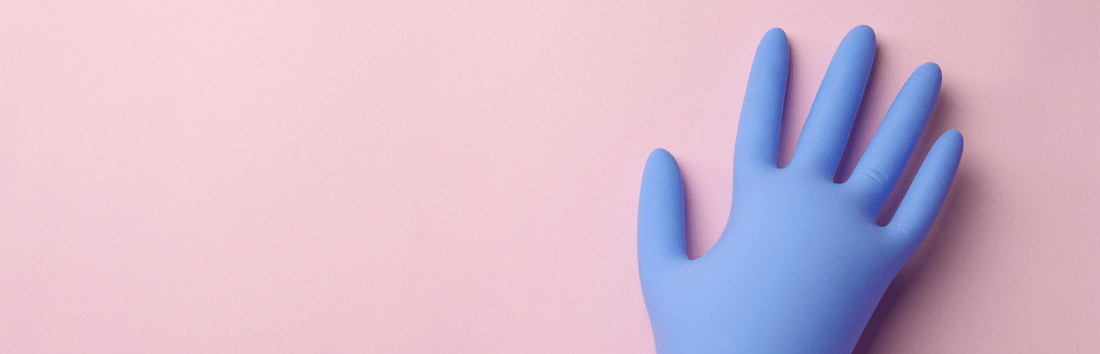 Blaue Einweghandschuh-Hand auf rosa Hintergrund, rechts im Bild platziert mit viel freiem Raum links