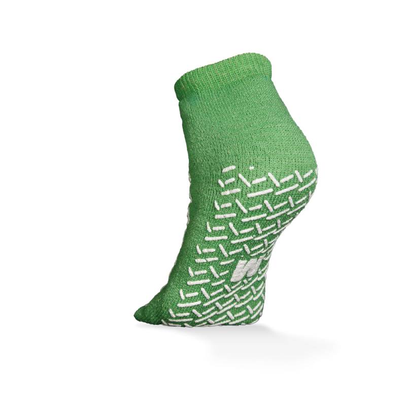 Die ECO-PLUS Anti-Rutsch Einwegsocken beidseitig beschichtet von AMPri Handelsgesellschaft mbH ist eine grüne Knöchelsocke mit weißen rutschfesten Griffen, dargestellt auf einem erhöhten Fuß vor weißem Hintergrund - ideal für medizinische Bereiche.