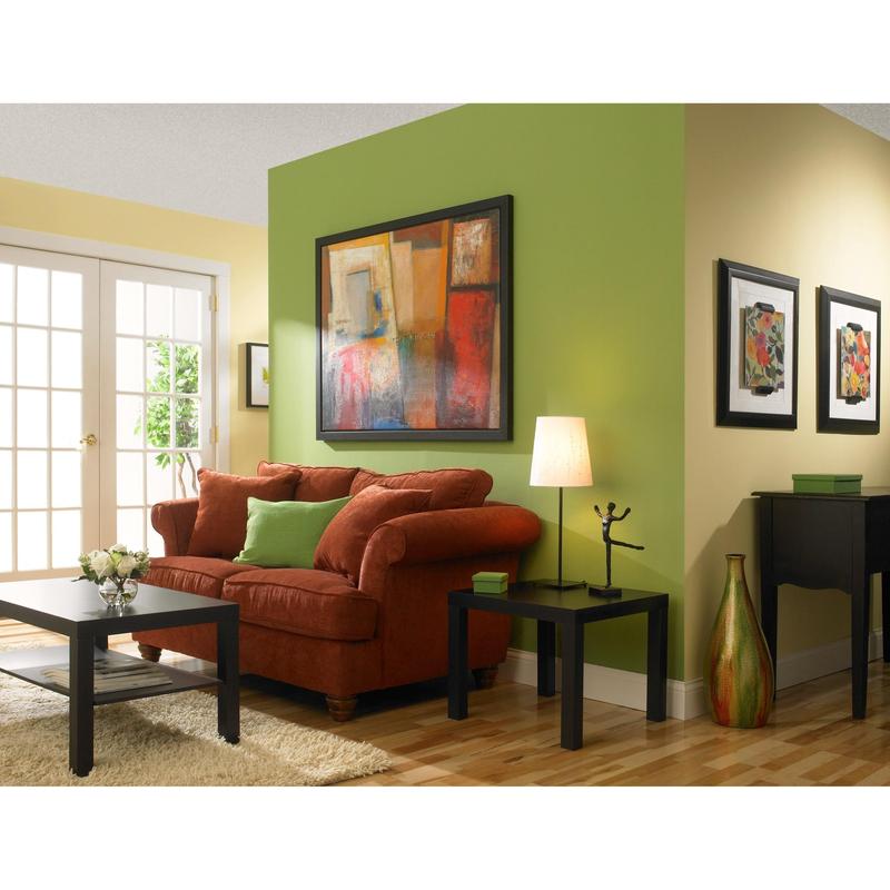 Ένα καθιστικό με κίτρινους και πράσινους τοίχους βαμμένους με ταινία κάλυψης ζωγράφων ScotchBlue™ "Multi-Surface" από την 3M Deutschland GmbH, έναν κόκκινο καναπέ με πράσινα μαξιλάρια, ένα μαύρο τραπεζάκι, ένα βοηθητικό τραπέζι με λάμπα, αφηρημένη τέχνη, ξύλινο πάτωμα και γυάλινες πόρτες.