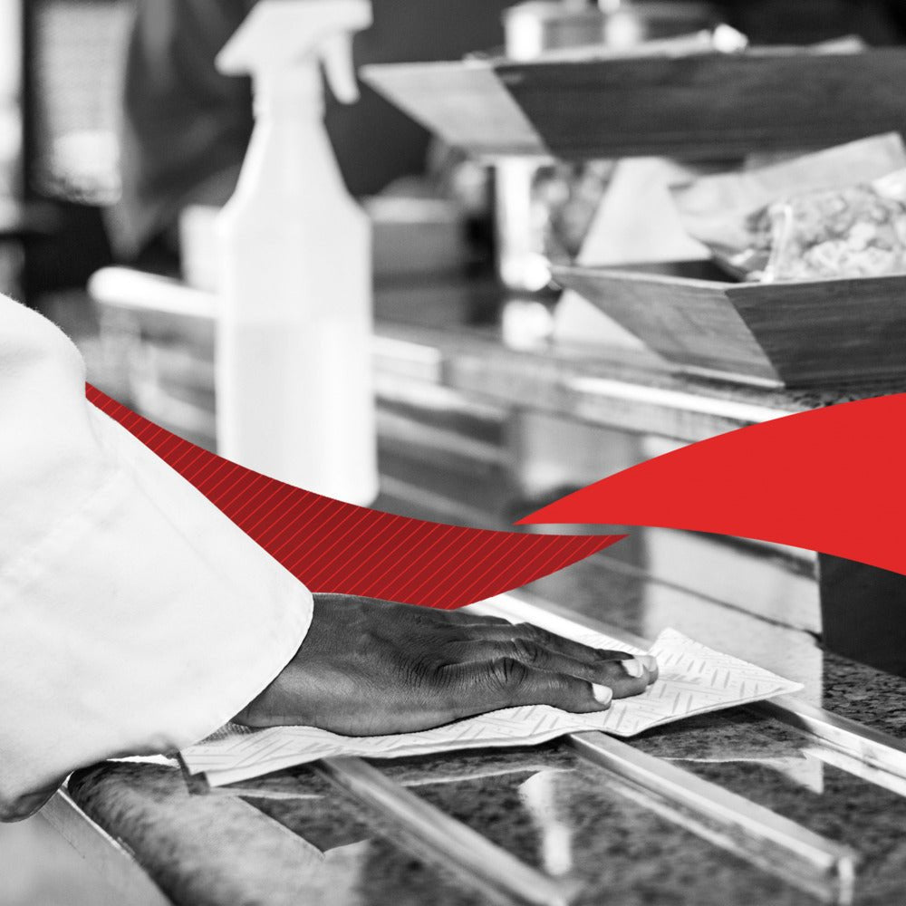 Ένα χέρι καθαρίζει μια επιφάνεια από γρανίτη με χαρτοπετσέτα WypAll® L20 (2-στρώσεων, 6 x 550 φύλλα) της Kimberly-Clark GmbH· πίσω φαίνεται ένα μπουκάλι ψεκασμού και μπολ με φαγητό, με ένα κόκκινο γραφικό στοιχείο να διασχίζει την εικόνα.