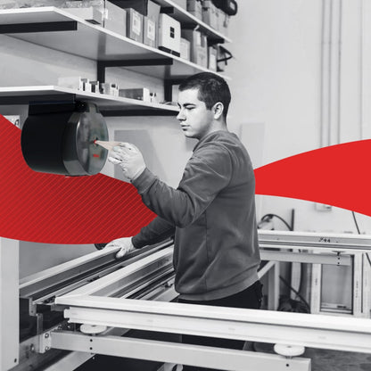 Σε ένα εργαστήριο, ένα άτομο αφαιρεί μια WypAll® L20 χαρτοπετσέτα από την Kimberly-Clark GmbH μέσω κεντρικής αφαίρεσης από τον τοίχο και καθαρίζει βιομηχανικές επιφάνειες εργασίας. ένα κόκκινο γραφικό στοιχείο διατρέχει το κέντρο της εικόνας.