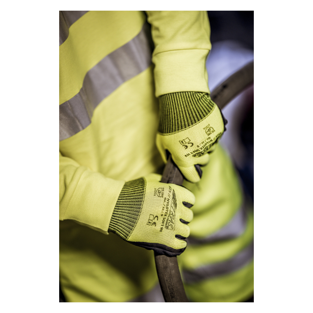Ένα άτομο που φοράει ένα κίτρινο γιλέκο ασφαλείας και γάντια από νάιλον NITRAS NYLOTEX SOFT HV της AS Arbeitsschutz GmbH, νεον κίτρινα, μερικώς επικαλυμμένα - με μαύρο κείμενο και σύμβολα ασφαλείας - κρατάει ένα παχύ, σκοτεινό καλώδιο ή σωλήνα.