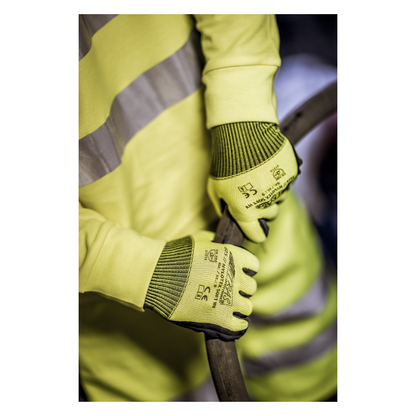 Ένα άτομο που φοράει ένα κίτρινο γιλέκο ασφαλείας και γάντια από νάιλον NITRAS NYLOTEX SOFT HV της AS Arbeitsschutz GmbH, νεον κίτρινα, μερικώς επικαλυμμένα - με μαύρο κείμενο και σύμβολα ασφαλείας - κρατάει ένα παχύ, σκοτεινό καλώδιο ή σωλήνα.