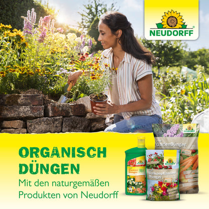 Eine Frau kniet in einem Garten und pflanzt Blumen in ein Hochbeet aus Stein. Im Vordergrund ist der Azet GartenDünger von Neudorff Shop zu sehen. Der deutsche Text hebt den ausgewogener Dünger für gesundes Pflanzenwachstum hervor.
