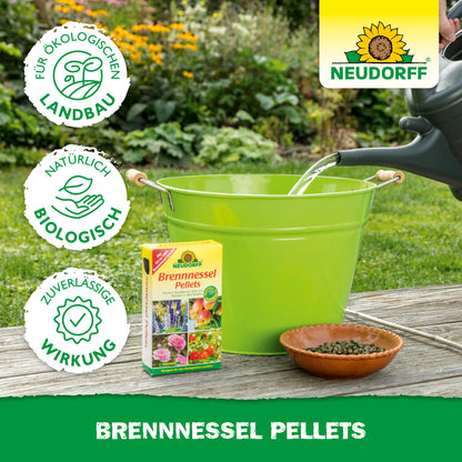 Ein grüner Eimer und eine braune Schale mit Neudorff Shop Brennnessel Pellets stehen im Freien. Eine Gießkanne füllt den Eimer, während eine Schachtel mit diesen Pellets daneben steht - perfekt als Pflanzenstärkungsmittel für Ihren Garten.