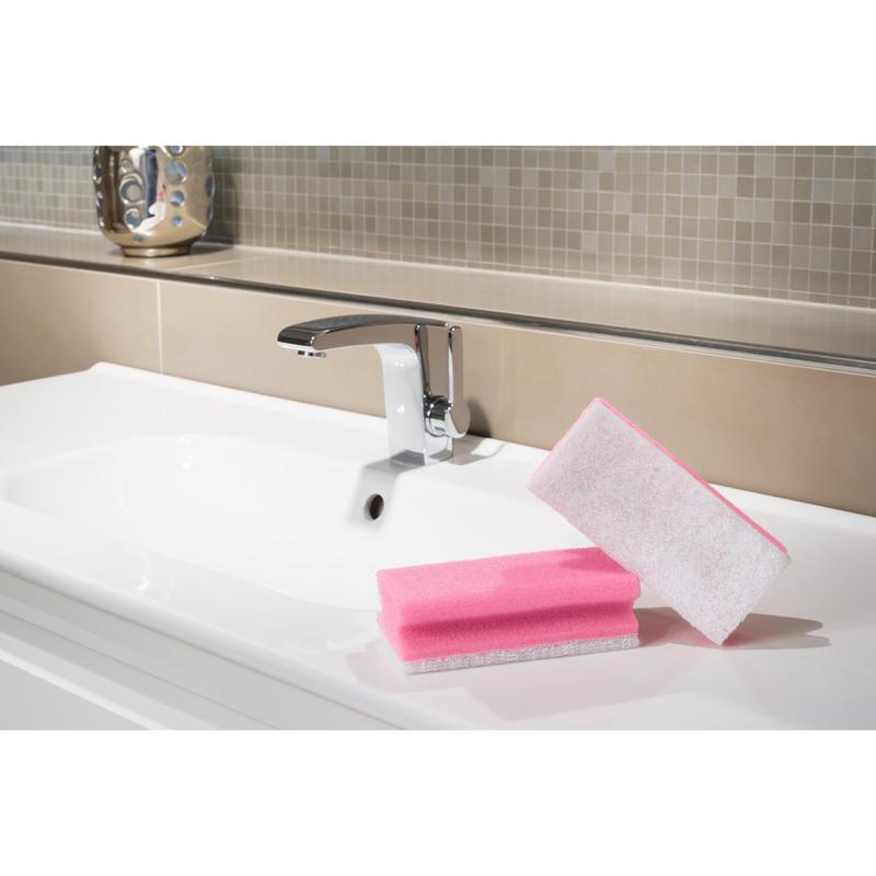 Ένα Scotch-Brite® Bath Griffschwamm XXL από την 3M Deutschland GmbH βρίσκεται στην άκρη ενός λευκού νιπτήρα με χρωμέ βρύση στο μπάνιο με μπεζ πλακάκια στο πίσω μέρος - ιδανικό για εύκολο καθαρισμό του μπάνιου.