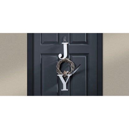 Eine schwarze Tür zeigt große weiße Buchstaben "J" und "Y" mit einem kleinen braunen Kranz - aufgehängt von einem 3M Deutschland GmbH Command™ transparenter, mittelgroßer, ovaler Haken (Außenbereich, 17091AW) - dazwischen, um "JOY" zu schreiben. Der Hintergrund ist eine schlichte hellbraune Wand.