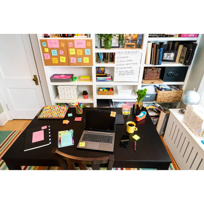 Ein Schreibtisch mit Laptop, Notizbüchern, Telefon, Stiften, Maus, gelber Tasse und Post-it® Super Sticky Z-Notes (Boost Collection) von 3M Deutschland GmbH. Dahinter befinden sich Regale mit Büchern, Aufbewahrungsboxen und ein Whiteboard mit Erinnerungshilfen und bunten Haftnotizen.