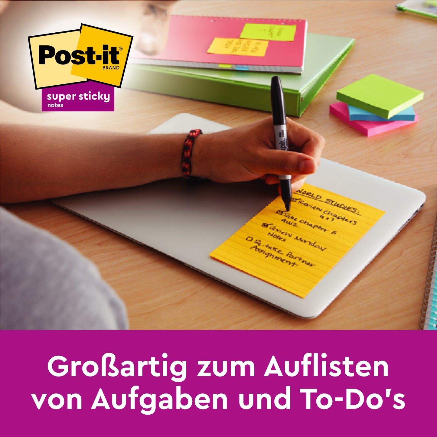 Eine Hand schreibt auf ein rosa Post-it® Super Sticky Notes im Großformat von 3M Deutschland GmbH, liniert (127 x 203 mm), auf einem geschlossenen Laptop. Weitere Haftnotizen und Stifte liegen daneben. Perfekt zum Listen Schreiben und Aufgaben-Planen.