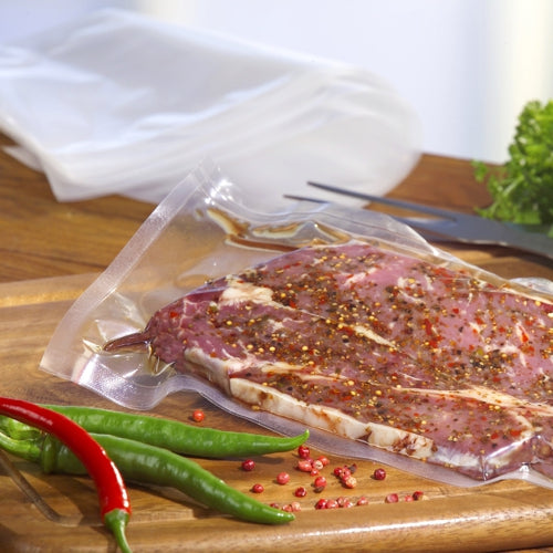 Ένας Starpak 100 Siegelrandbeutel, PA/PE διαφανής από Starpak κρατά μαριναρισμένο ωμό κρέας πάνω σε ένα ξύλινο σανίδι με πιπεριές τσίλι και πράσινα λαχανικά - ιδανικός για κενό τροφίμων με θάλαμο κενού.