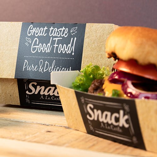 Ένας δίσκος από χαρτόνι με την επιγραφή "Snack A La Carte" περιέχει ένα χάμπουργκερ με μαρούλι, ντομάτα και κρεμμύδι. Στο παρασκήνιο υπάρχει μια PAPSTAR 50 κουτιά burger, χαρτόνι "pure" "Good Food" της PAPSTAR GmbH: Καλή γεύση Good Food! Καθαρό & Νόστιμο.
