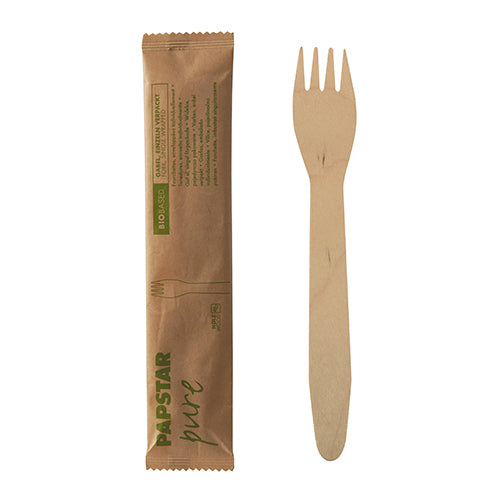 Μια ξύλινη PAPSTAR πιρούνα "pure", 15,5 cm, συσκευασμένη μεμονωμένα σε συρρικνωμένο φιλμ (50 τεμάχια), βρίσκεται δίπλα στην κλειστή καφέ συσκευασία της από την PAPSTAR GmbH με πράσινη εκτύπωση και απλό σχέδιο.