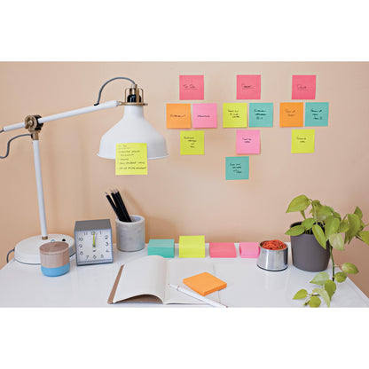 Ein aufgeräumter Schreibtisch mit Lampe, Uhr, Pflanze, Stifthalter, einem aufgeschlagenen Notizbuch und Stiften. An der Wand über dem Schreibtisch sind bunte Post-it® Notes Würfel Ultra-Farben von 3M Deutschland GmbH für handschriftliche Erinnerungen und Aufgaben angebracht.