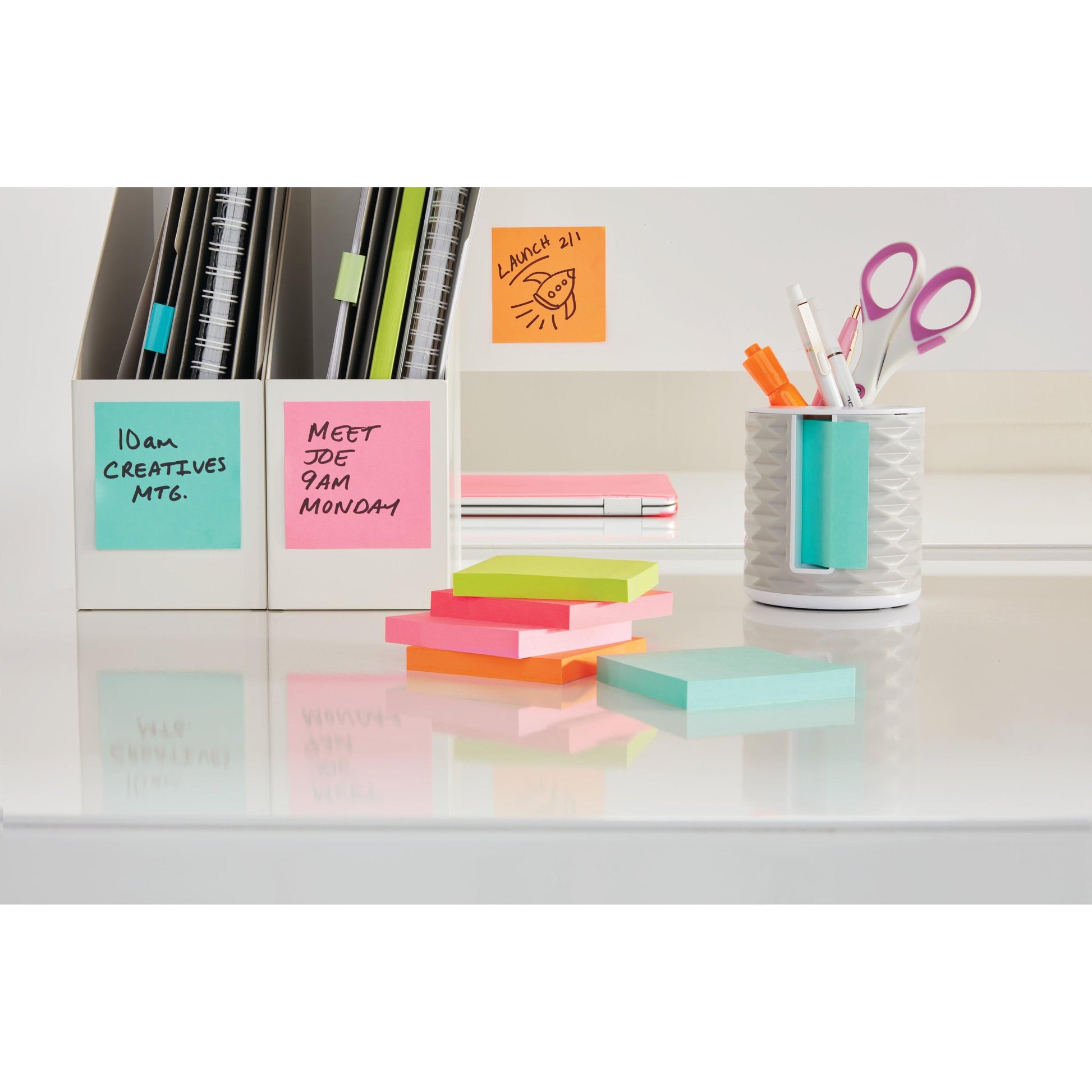 Ein aufgeräumter Schreibtisch mit 3M Post-it® Super Sticky Z-Notes in Neonfarben (76x127mm, 100 Blatt/Block, 6 Blöcke/Packung, PEFC-zertifiziert) sowie Stiften, Scheren, Notizbüchern und Aktenordnern. Die Zettel zeigen handschriftliche Erinnerungen auf einer reflektierenden Oberfläche.