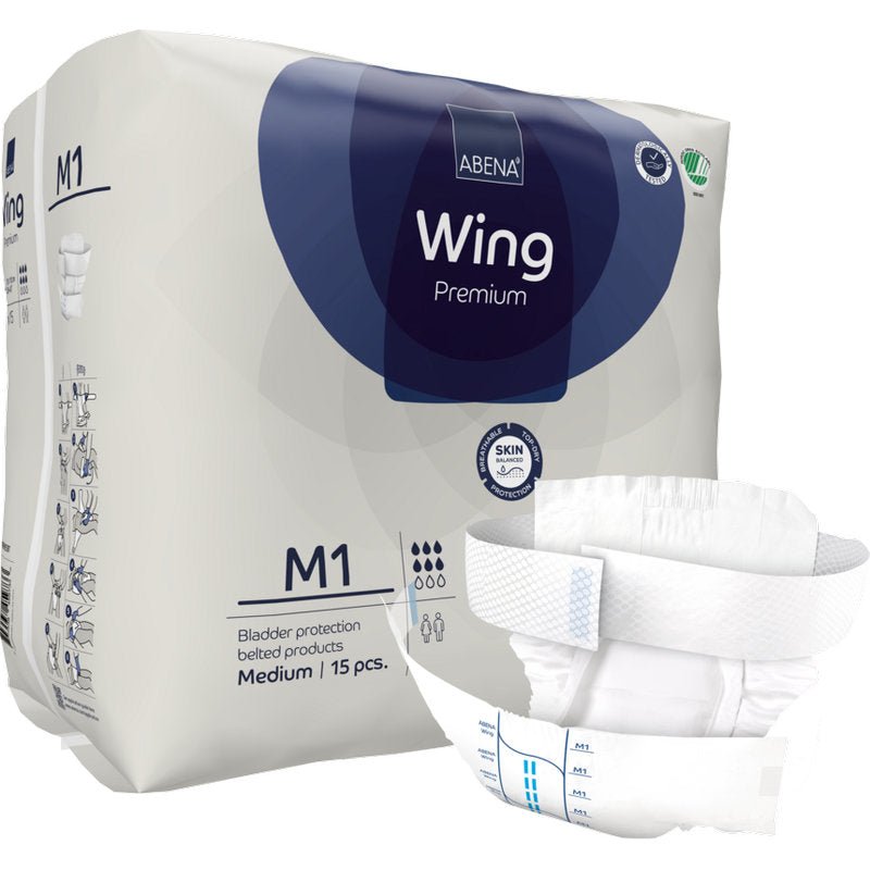 Μια συσκευασία Abena Re-Seller GmbH ABENA Wing Premium απεικονίζεται με ένα ανοιγμένο μαξιλάρι μπροστά που προσφέρει προστασία και άνεση. Στη συσκευασία αναφέρεται ότι περιέχει 15 μεσαίου μεγέθους μαξιλάρια για προστασία της ουροδόχου κύστης.