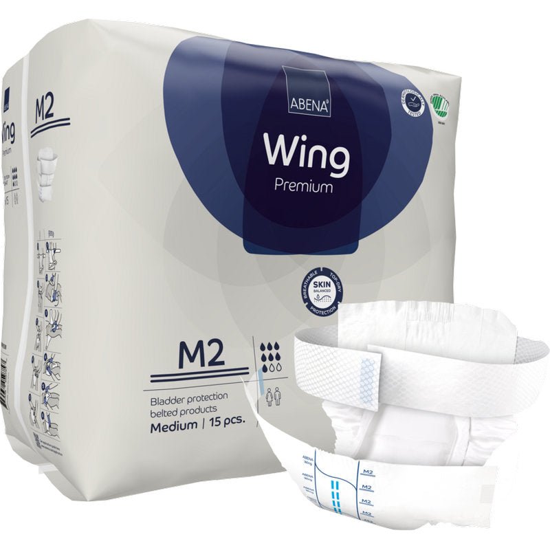 Παρουσιάζεται ένα πακέτο της Abena Re-Seller GmbH ABENA Wing Premium που περιέχει 15 μεσαίου μεγέθους προϊόντα ακράτειας με ζώνη. Μπροστά απεικονίζεται ένα προϊόν που τονίζει την απόλυτη προστασία για ενήλικες.