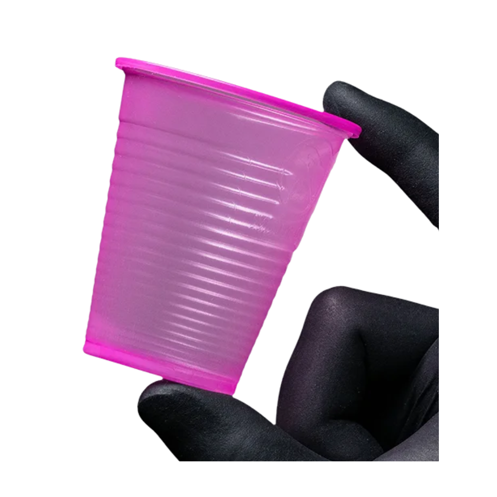 Ένα μικρό, ροζ ποτήρι AMPri Dental PP από πολυπροπυλένιο κρατιέται ανάμεσα σε δύο γαντοφορεμένα δάχτυλα μπροστά από ένα λευκό φόντο. Αυτό το ποτήρι μιας χρήσης της AMPri Handelsgesellschaft mbH, που βρίσκεται συχνά σε οδοντιατρεία, έχει υφή επιφάνειας με οριζόντιες ραβδώσεις.