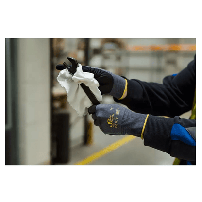 Ένα άτομο με AMPri SolidSafety Tough Air υπερελαφριά γάντια συναρμολόγησης της AMPri Handelsgesellschaft mbH καθαρίζει προσεκτικά έναν κλειδί με ένα λευκό πανί σε εσωτερικό χώρο. Τα γκρι γάντια, που είναι γνωστά για το επίπεδο αντοχής στην τριβή 4, ξεχωρίζουν από τα θολά βιομηχανικά ράφια και συσκευές στο παρασκήνιο.