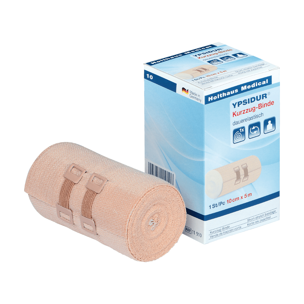Ypsidur® ελαστικός επίδεσμος με κλιπ από την Holthaus Medical GmbH & Co. KG. Η εικόνα δείχνει έναν τυλιγμένο μόνιμα ελαστικό επίδεσμο δίπλα στο κουτί του. Ο μπεζ επίδεσμος είναι στερεωμένος με δύο μπεζ κλιπ, και το κείμενο στο κουτί είναι κυρίως στα γερμανικά και περιέχει λεπτομέρειες προϊόντος.