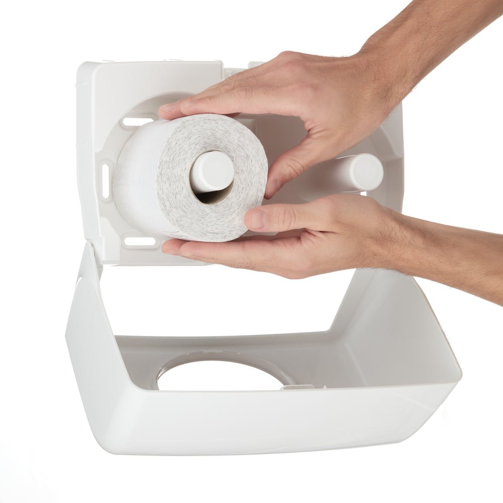 Ένα άτομο τοποθετεί ένα νέο ρολό χαρτιού τουαλέτας Kleenex® μικρού μεγέθους από μια συσκευασία 8 x 12 της Kimberly-Clark GmbH σε έναν λευκό πλαστικό διανομέα με ανοιχτό καπάκι.