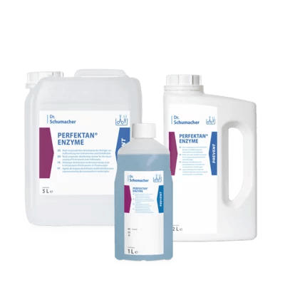 Τρία λευκά πλαστικά δοχεία της Dr. Schumacher GmbH PERFEKTAN® ENZYME (5L, 2L, 1L) - με μπλε και μοβ ετικέτες - είναι εκτεθειμένα, ιδανικά για τον ενζυματικό καθαρισμό ιατρικών εργαλείων.