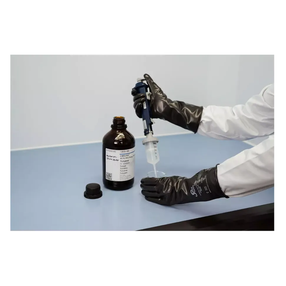 Ένα άτομο που φοράει AMPri SolidSafety ChemV Full Stabile Brom-Butyl-Chemikalienschutzhandschuhe με εξωτερικό στρώμα Viton και ένα λευκό εργαστηριακό παλτό, απορροφά υγρό από μια καφέ φιάλη με μια πιπέτα σε μια ανοιχτό γκρι επιφάνεια. Το καπάκι βρίσκεται κοντά στον εργαστηριακό χώρο εργασίας και διασφαλίζει τη χημική αντοχή κατά το χειρισμό ουσιών.