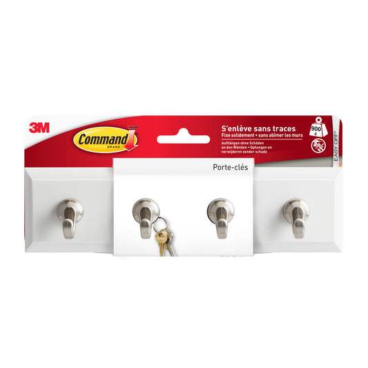 Eine Packung der Command™ Schlüsselleiste in Quarz, HOM18-Q von 3M Deutschland GmbH wird mit drei Metallhaken zur Schlüsselaufbewahrung gezeigt. Die Schlüssel hängen am mittleren Haken, und das französische Etikett weist auf die einfache und schnelle Installation hin.