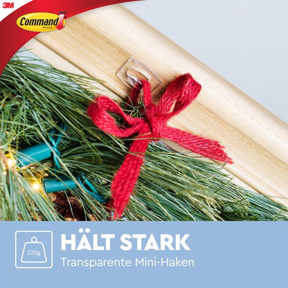 Ένας Command™ Mini-Haken, διαφανής (3M Deutschland GmbH), τοποθετείται χωρίς υπολείμματα σε ξύλο και κρατάει ένα δεμάτι κλαδιών πεύκου με κόκκινη κορδέλα (μέχρι 225g). Κείμενο: "ΚΡΑΤΑΕΙ ΔΥΝΑΤΑ Διαφανείς Mini-Haken".