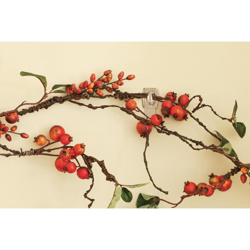 Ένα διακοσμητικό κλαδί με κόκκινα μούρα και πράσινα φύλλα κρέμεται σε μπεζ τοίχο, υποστηριζόμενο από το Command™ Mini-Haken, transparent, mit transparenten Strips, 17006CLRFGN von 3M Deutschland GmbH - τέλεια αποθήκευση χωρίς τρύπημα.